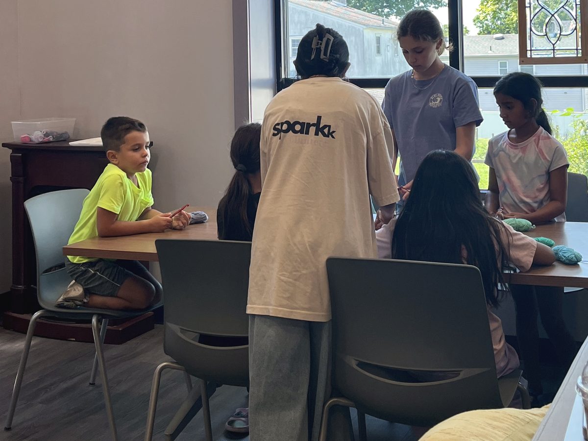 A volunteer in a sparkk shirt helping at the table during a free crochet class.